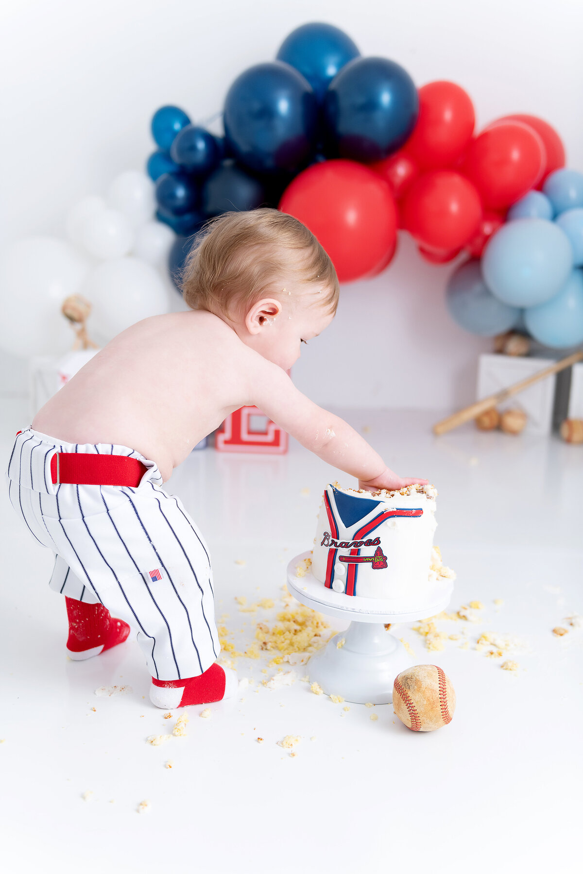 A toddler in baseball pants and socks smashes a Braves themed cake in a studio