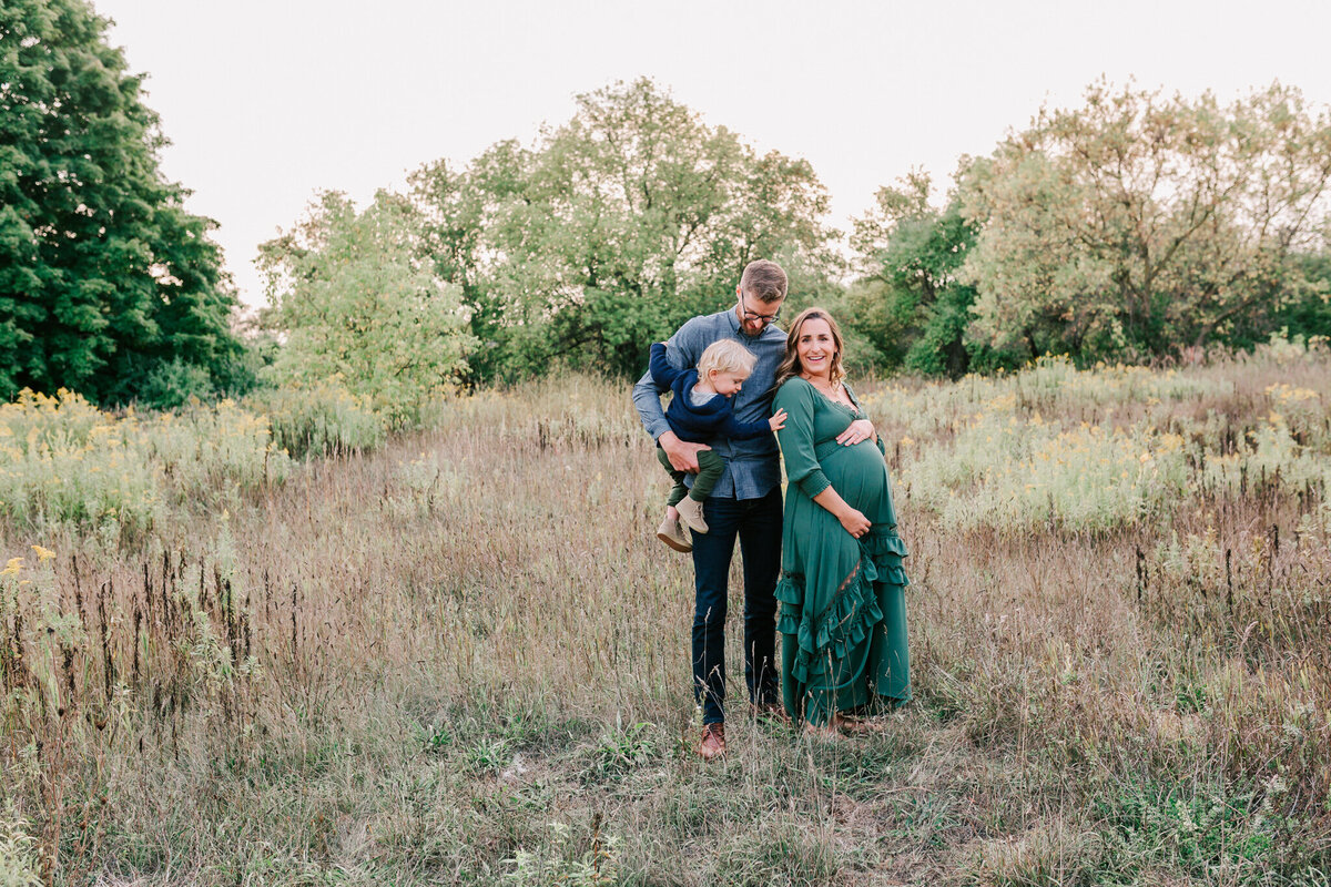 Family of three, soon to be four stand in a field for her maternity session.