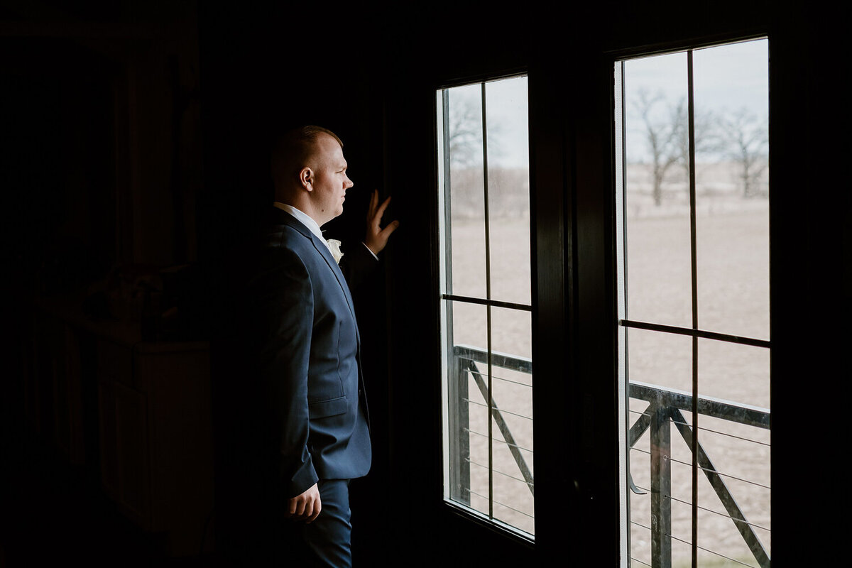 groom-window-portrait-wedding-day-moment-ashton-hill-farm-cedar-rapids-iowa-storyteller-collective-photo-co