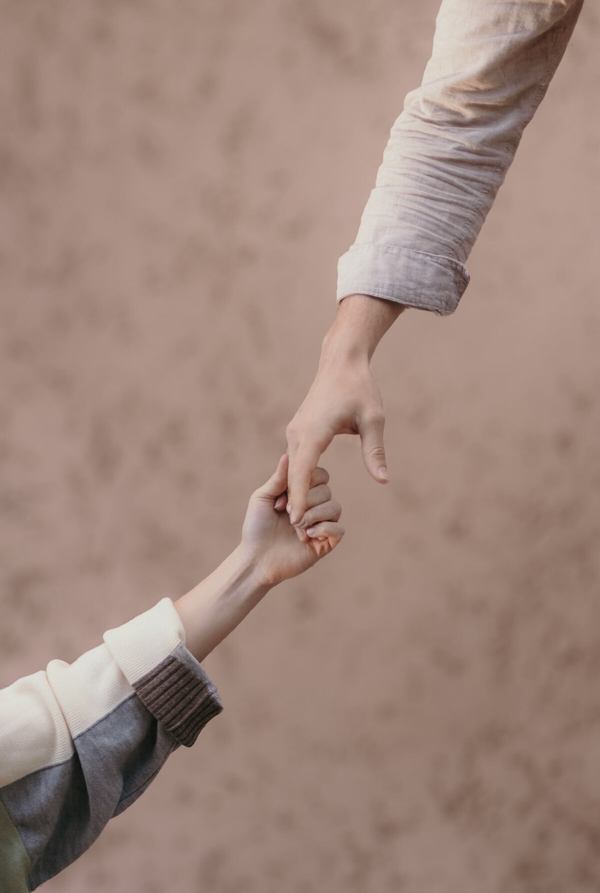 Closeup of to hands holding each other in front of a brown wall.