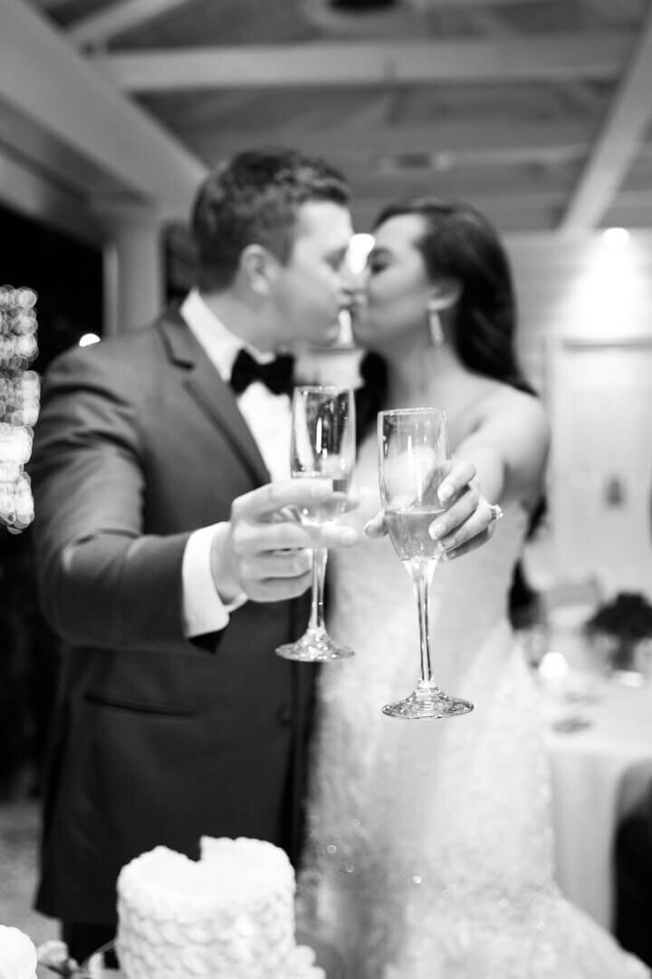 B&W image of bride and groom kissing while toasting at the reception.