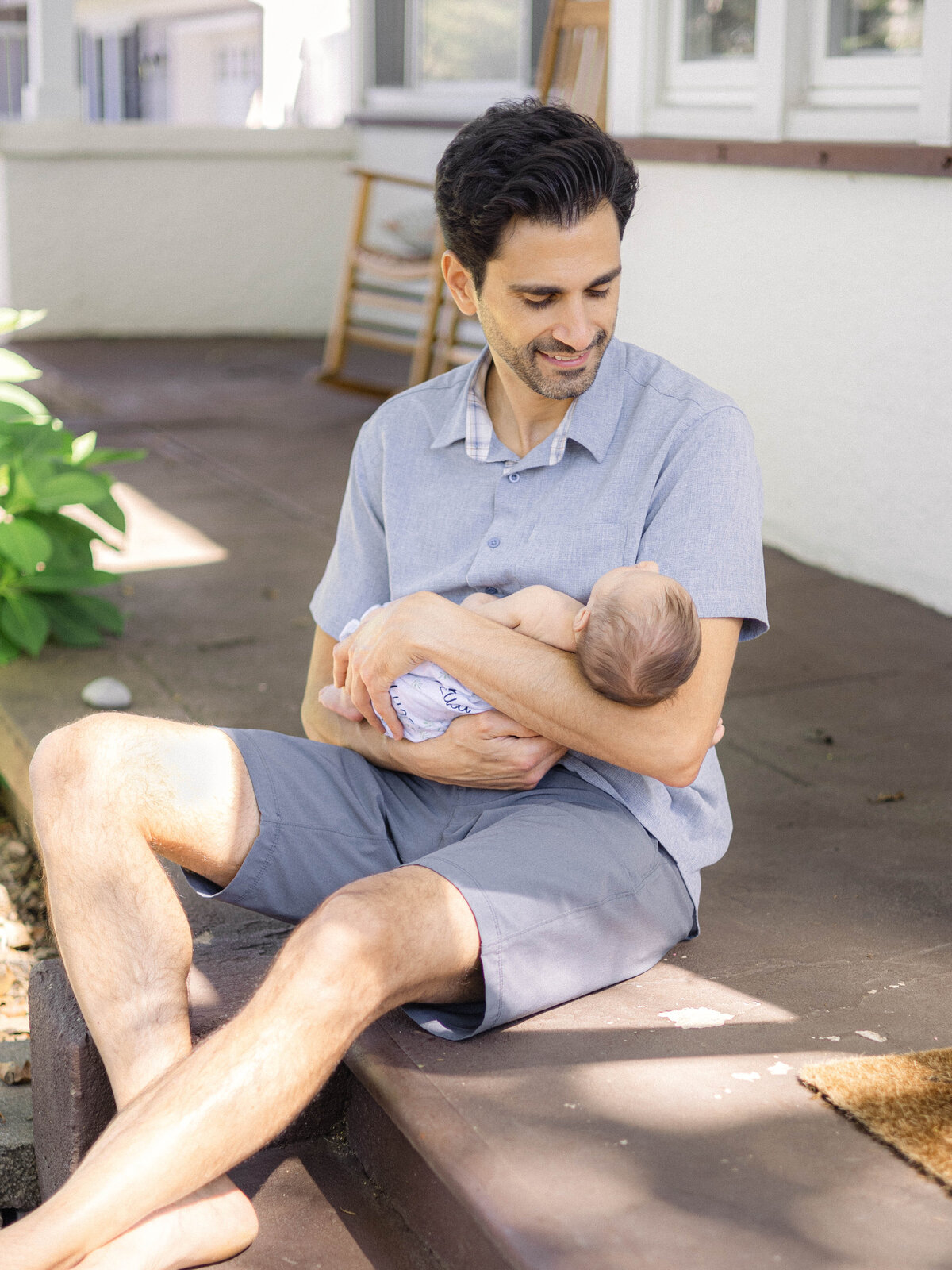 Dad gazing down at his newborn son on the front steps of their Tudor style family home.