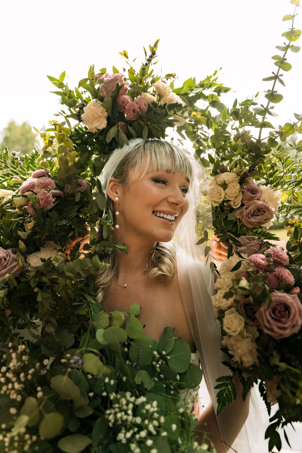 A bride smiles surrounding by flowers representing bridal makeup done by Looks with Libby.
