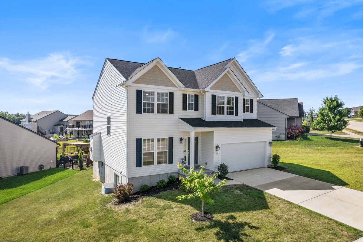 Drone photo at an angle, showing the front and left side of a white home with black shutters. For a real estate listing.