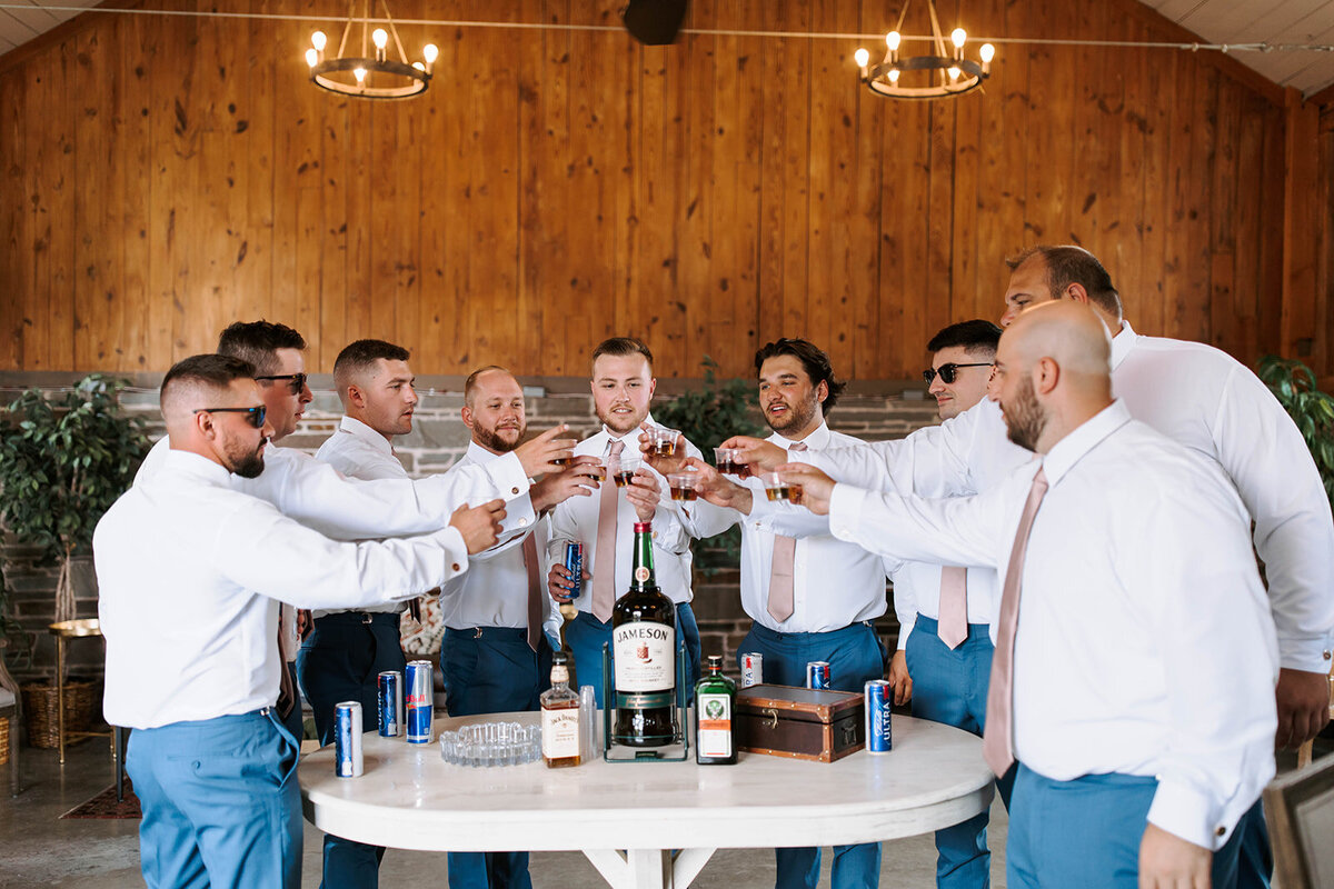 groomsmen in white barn getting ready taking a shot before ceremony