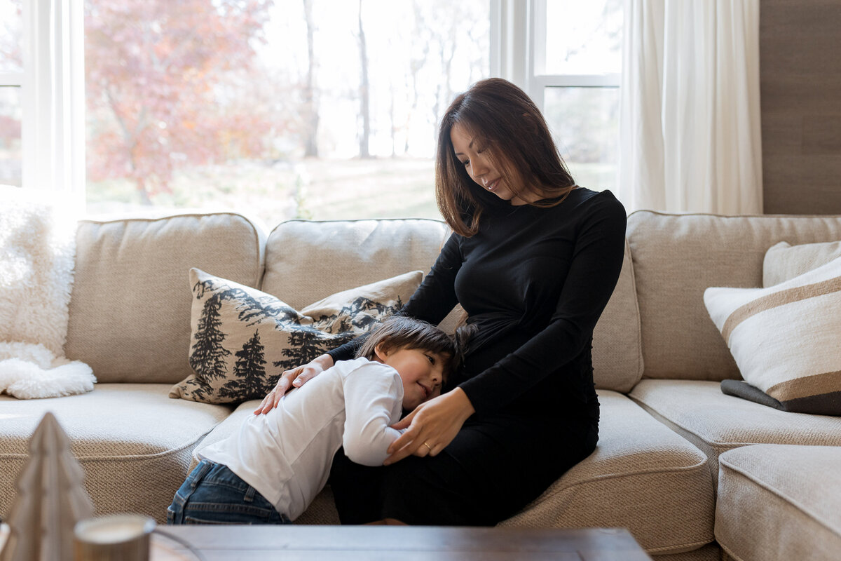 Maternity Photographer, a little boy hugs his mother on the couch, she is expecting another