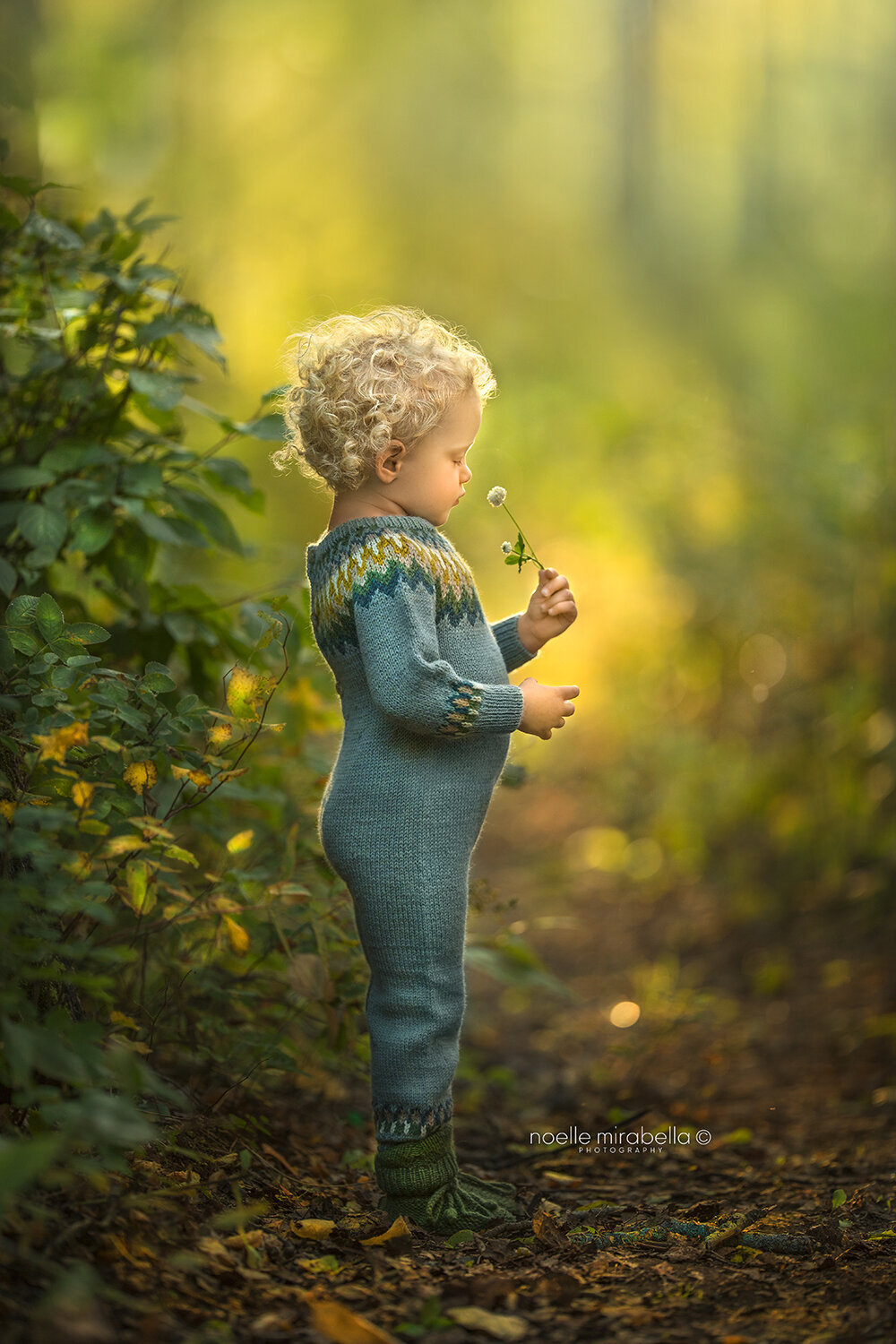 Child smelling clover outside on a forest trail in the sunlight.