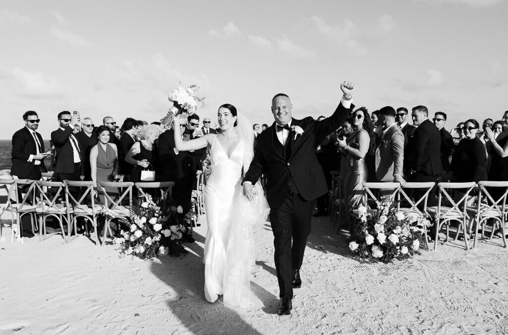 A triumphant moment as the bride raises her bouquet while walking down the aisle with her groom, celebrating their union. Captured by Claudia Amalia Photography, a Florida Keys wedding photographer.