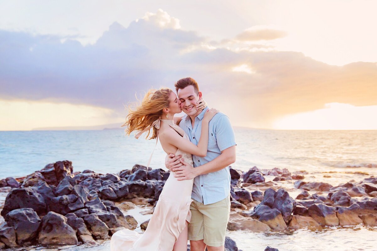 Woman kisses her boyfriend's cheek after he proposes to her on the beach in Maui