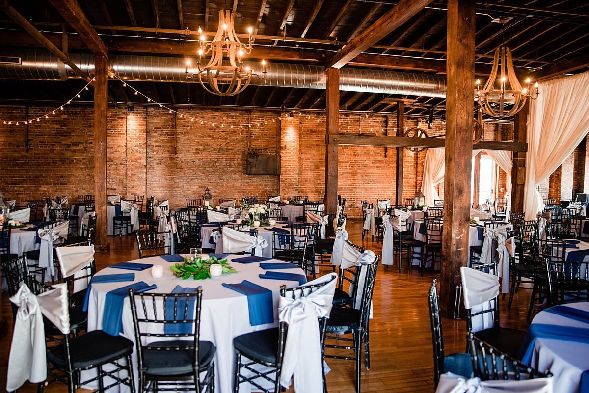 View of room inside of Cannery set up for a reception with round tables, bistro lights and draping