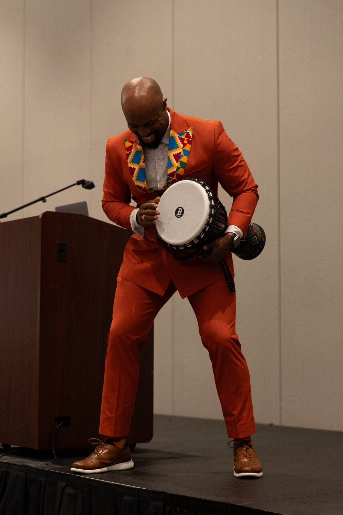 A person in an orange suit on a stage holding a drum 
