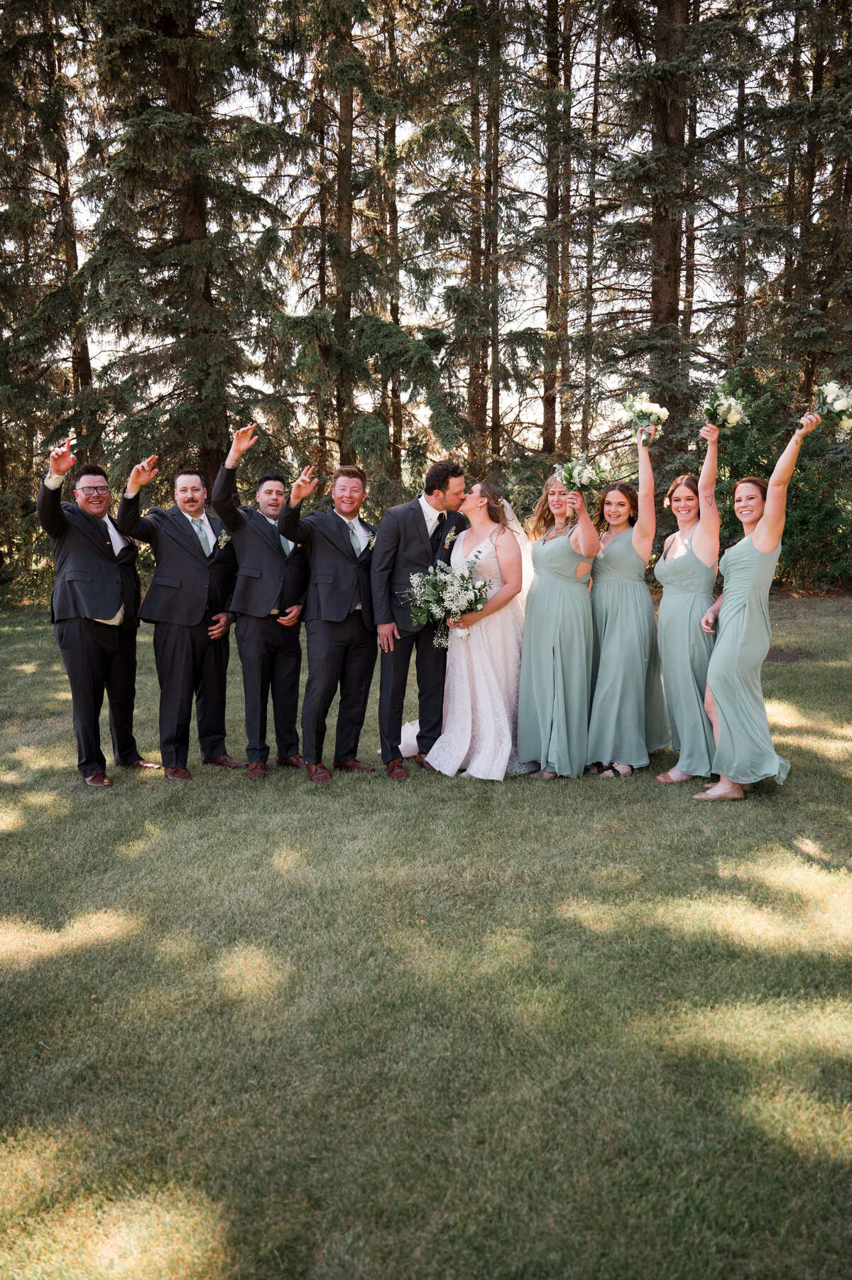 wedding party celebrating with couple in a field with trees in the background 
