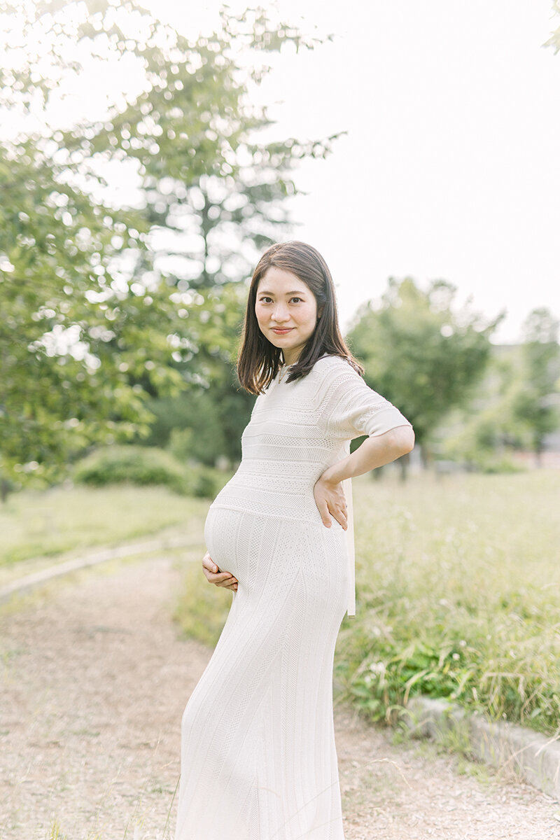 青葉区の緑の公園でおなかに手を当ててポーズをしている妊婦さんの美しく、おしゃれなまなにてぃフォト