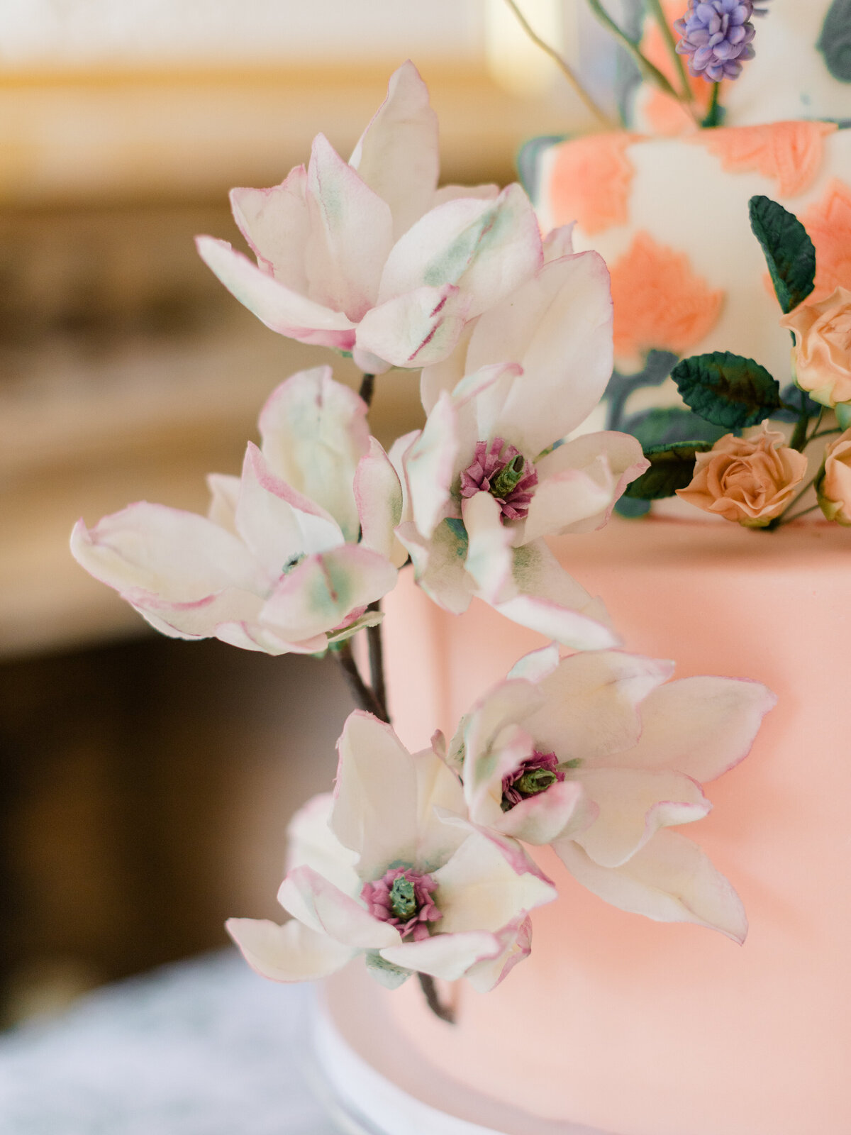 Close-up of hand-sculpted sugar magnolias with soft blush and sage accents, adorning a pastel pink wedding cake at Cairnwood Estate. Captured by Elizabeth Kane Photography, Philadelphia Fine Art Wedding Photographer, this detail showcases the artistry and romantic sophistication of luxury wedding design.