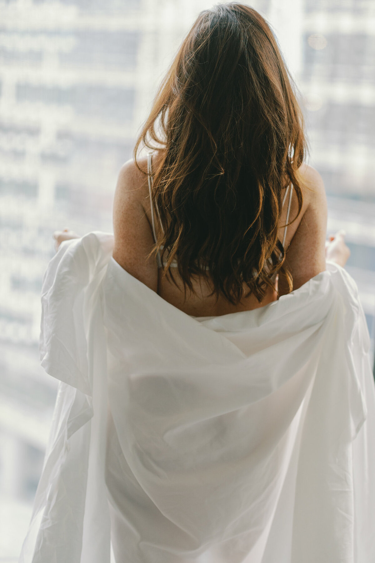 A woman wraps herself in hotel sheets for a boudoir photo in downtown Chicago