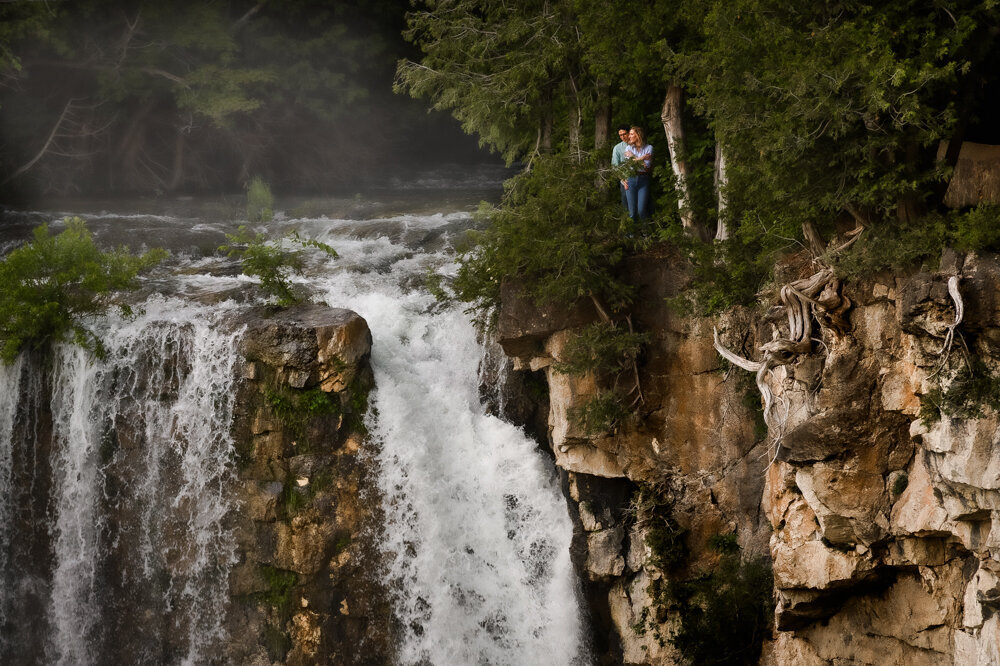 couple standing on cliff next to falls