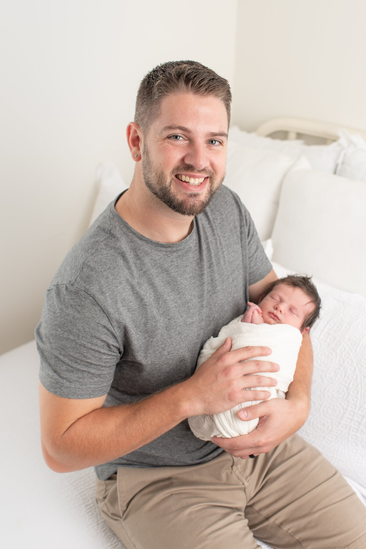 Father smiling at the camera, holding newborn son