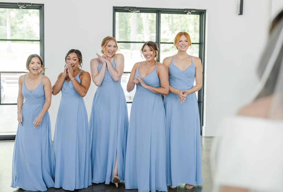 Bridesmaids in blue dresses giggle and cheer for bride in her dress