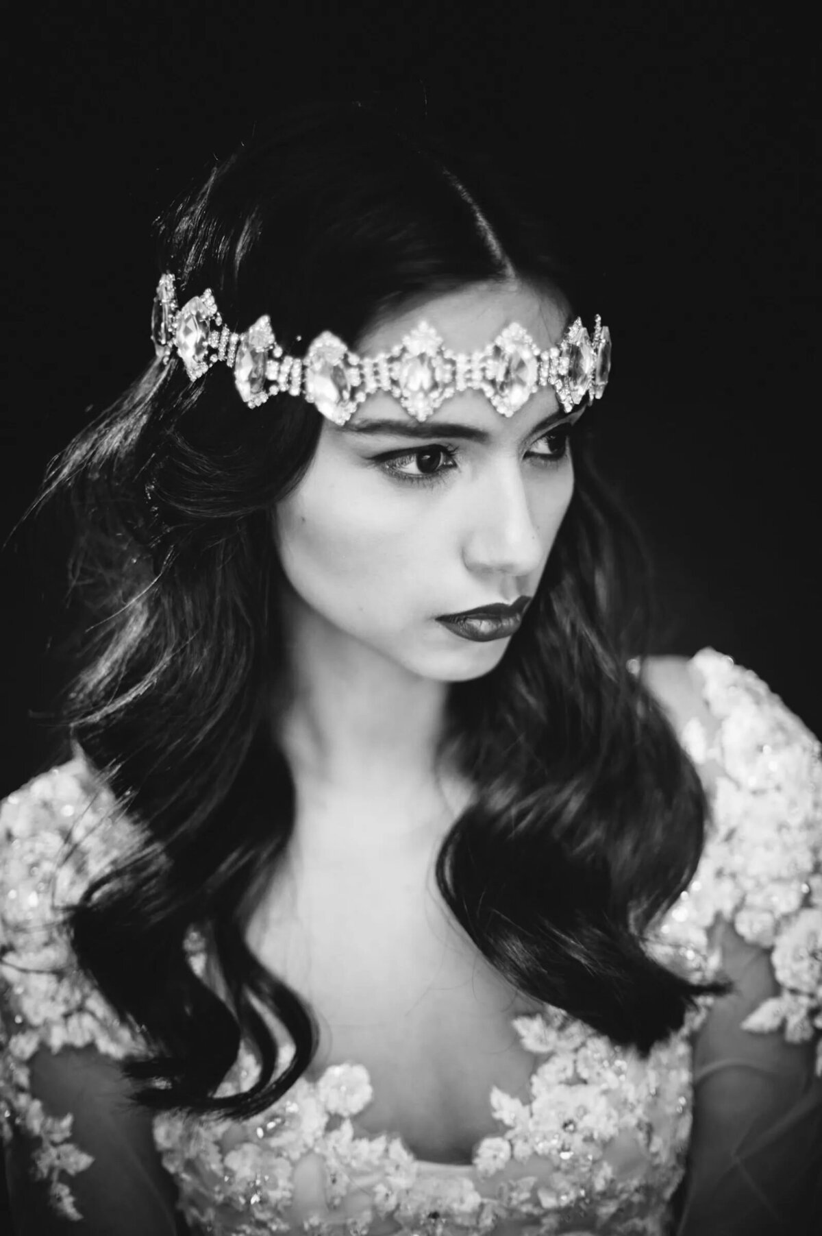 A close-up black and white portrait of a bride, her gaze intense and focused, adorned with a detailed headpiece and embellished dress.