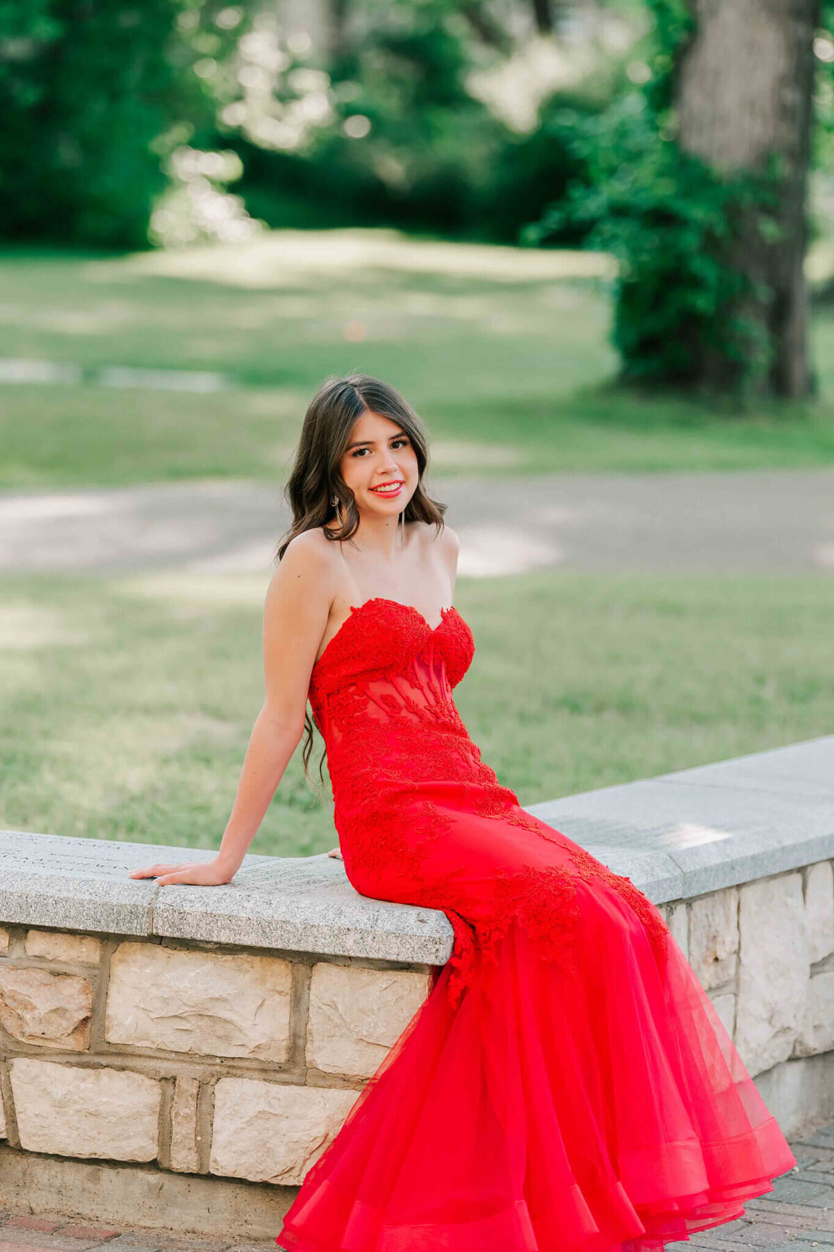 A young lady in a red dress sitting on a low stone wall