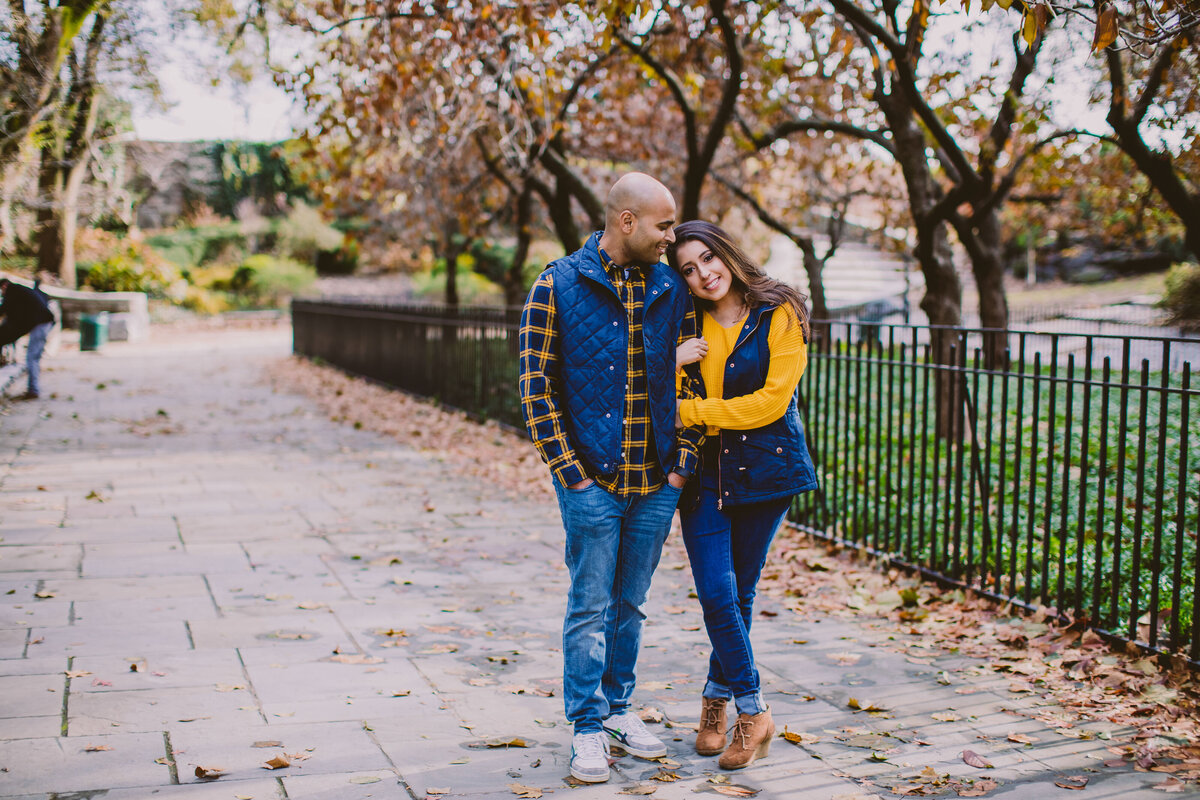 A couple standing on a walkway in carl schurz park in fall clothing in the autumn