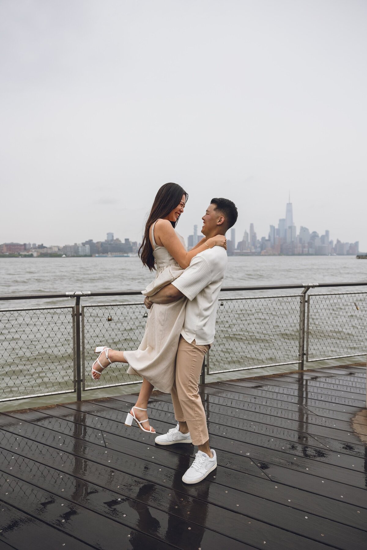 Groom-to-be lifting bride-to-be off the ground on rainy pier