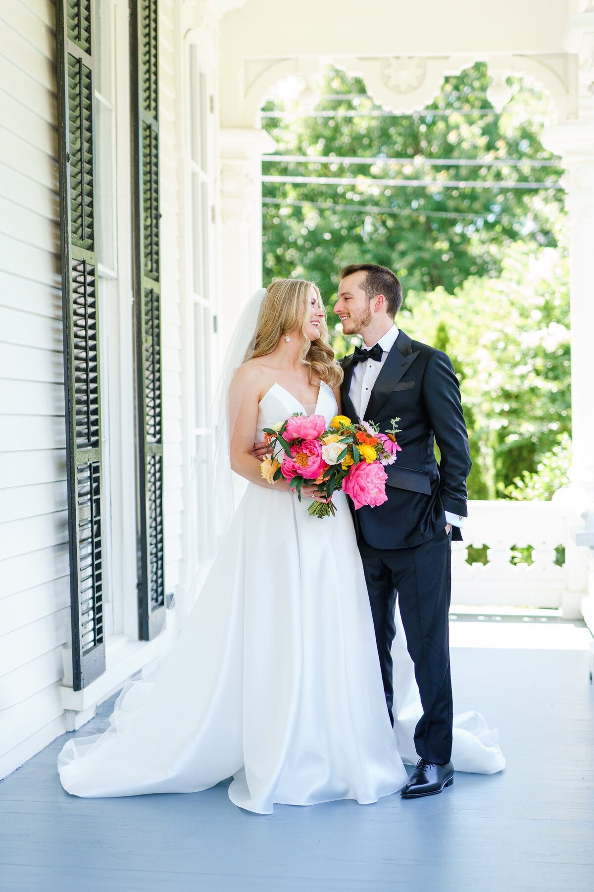 A bride and groom look at one another and smile on the front porch of Merrimon Wynne in Raleigh, NC.