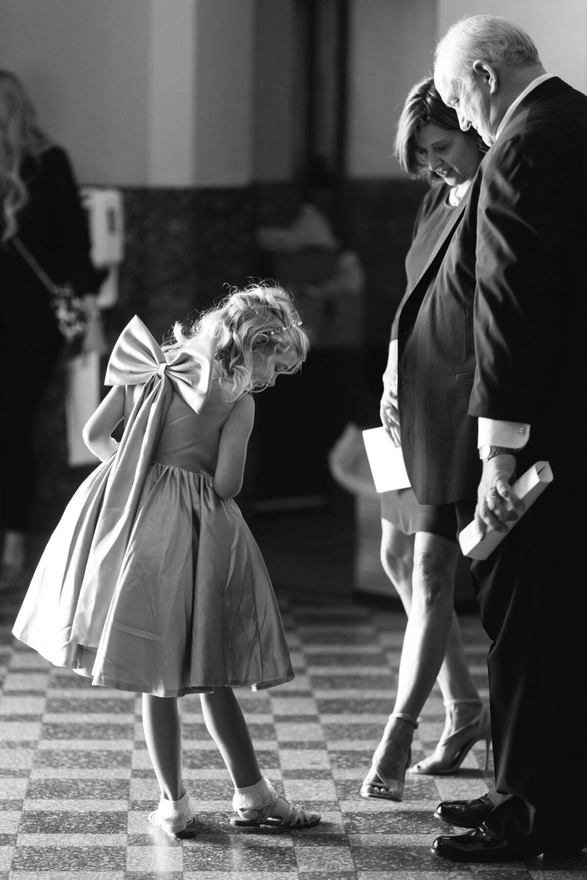 Black and white image of little girl showing off shoes to wedding guests