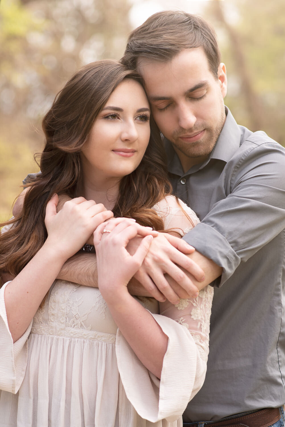 Engagement photo of a couple embracing in a natural outdoor setting, with the man hugging his fiancée from behind.