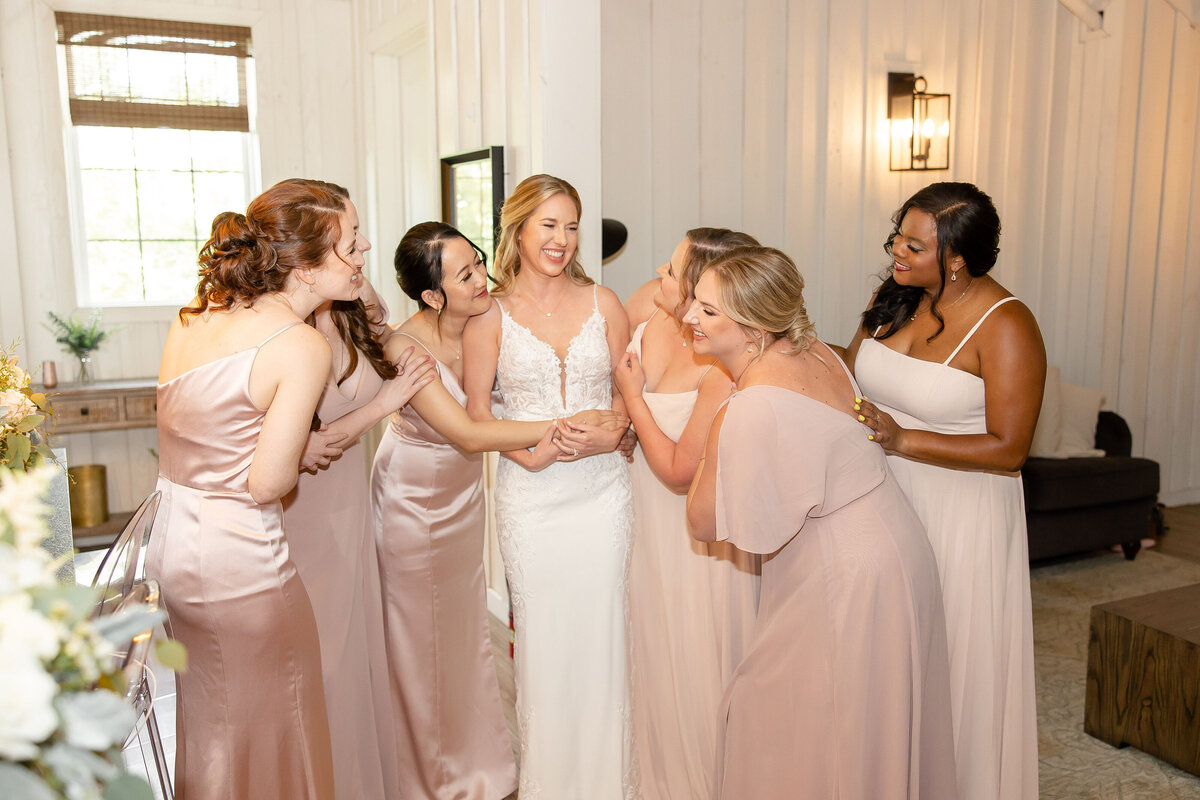 bridesmaids hug bride in suite with laughs and smiles pink dresses
