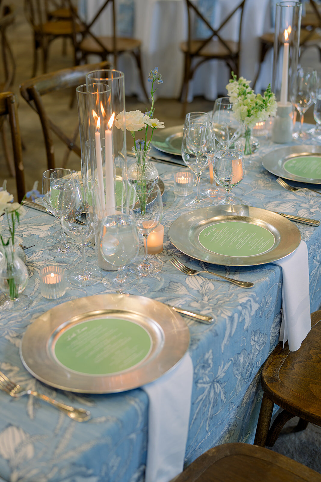 Toile patterned blue linen with candles and delicate florals at elegant wedding dinner setup.