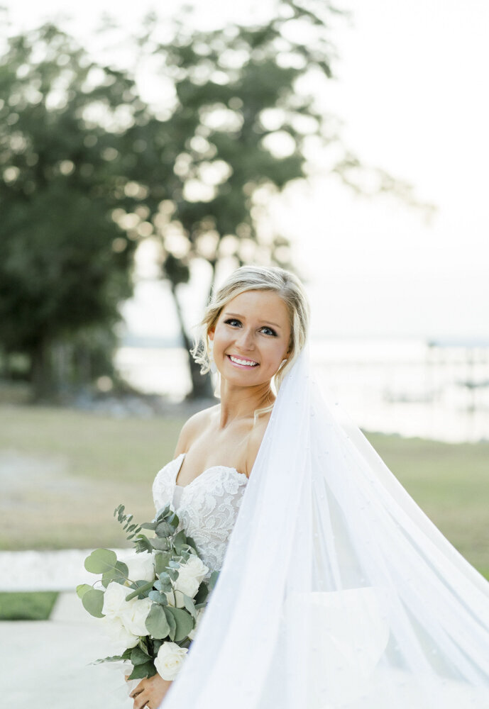bride smiling and holding a flower bouquet with veil behind her