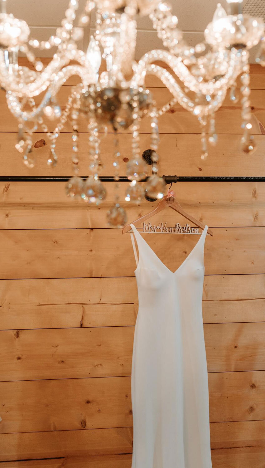 Simple white wedding dress on a hanger against a wooden wall