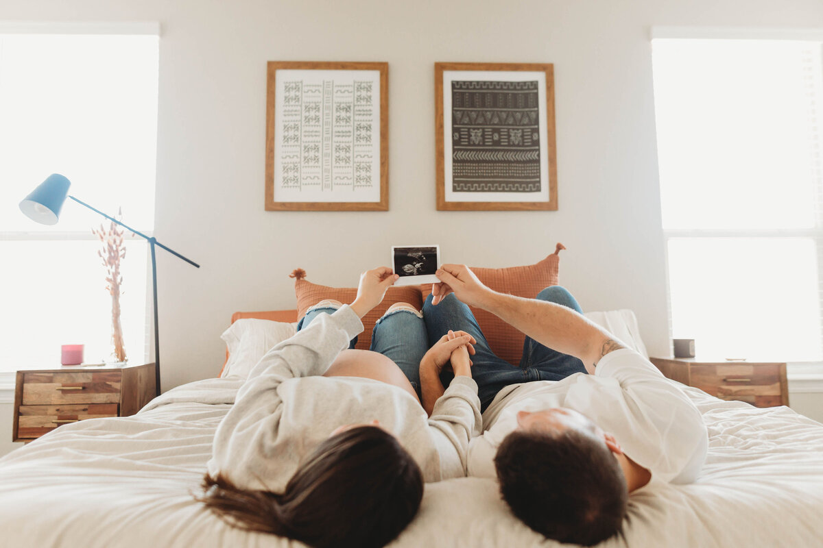 Couple laying on their bed holding up a sonogram print