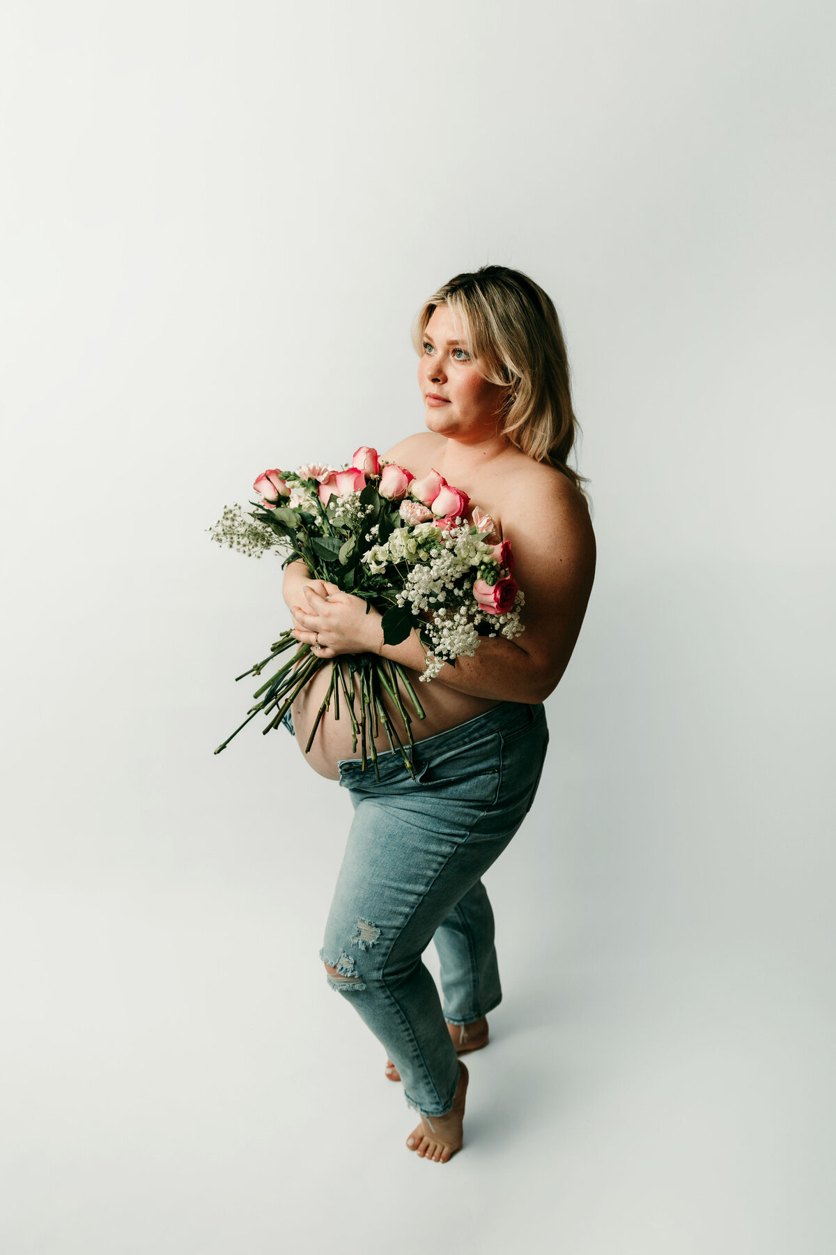 A mom shows off her pregnant belly while holding a bouquet of flowers to her chest.