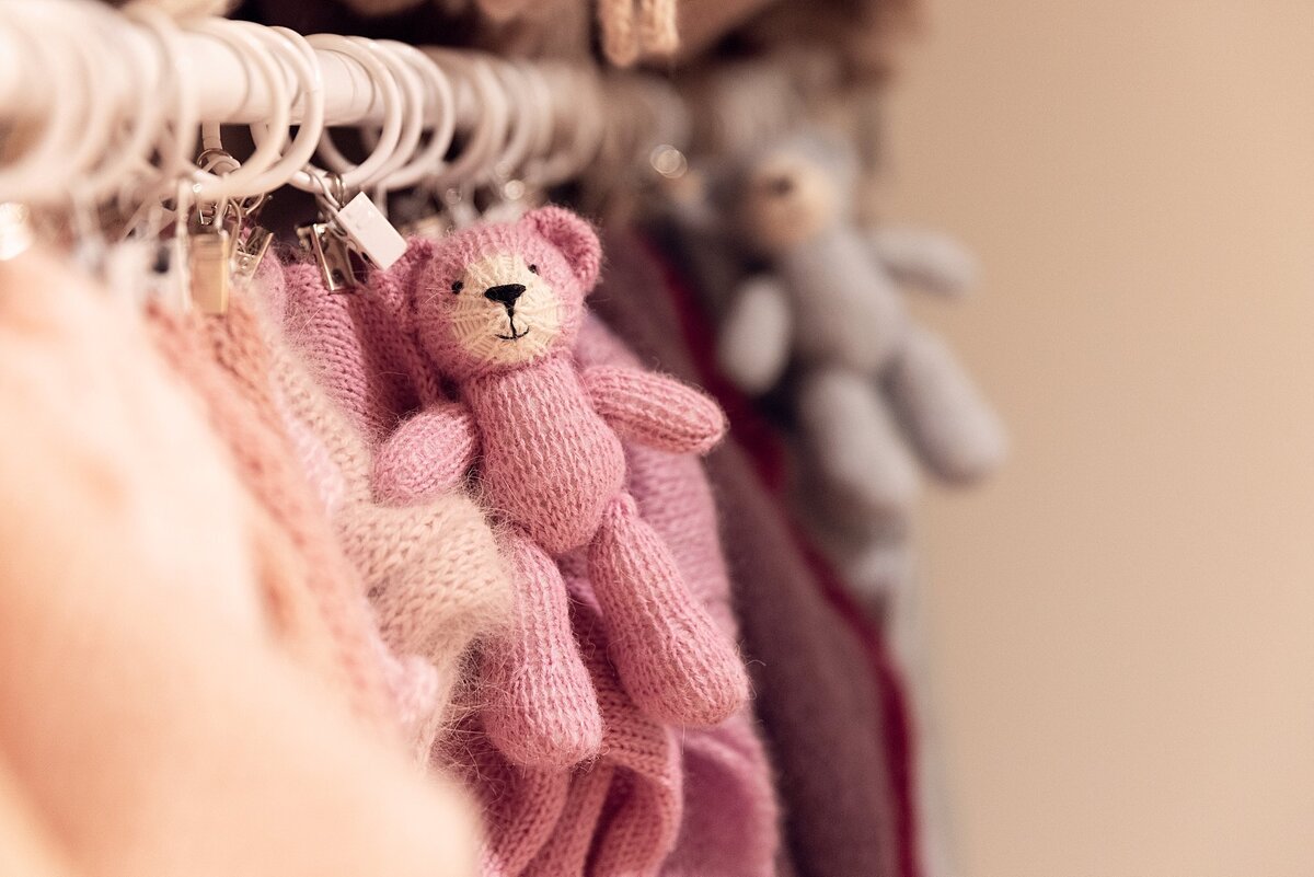 Close-up of hanging knit props and stuffed animals used in newborn photography sessions, arranged on a white rack.