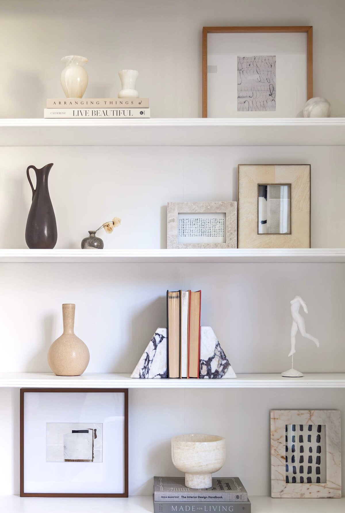 A beautifully styled bookshelf featuring sculptural ceramics, marble bookends, and framed artwork, creating a modern and sophisticated aesthetic. This elevated bookshelf styling blends neutral tones and rich textures, perfect for luxury home design in Short Hills, Montclair, Summit, Chatham, and Ridgewood.