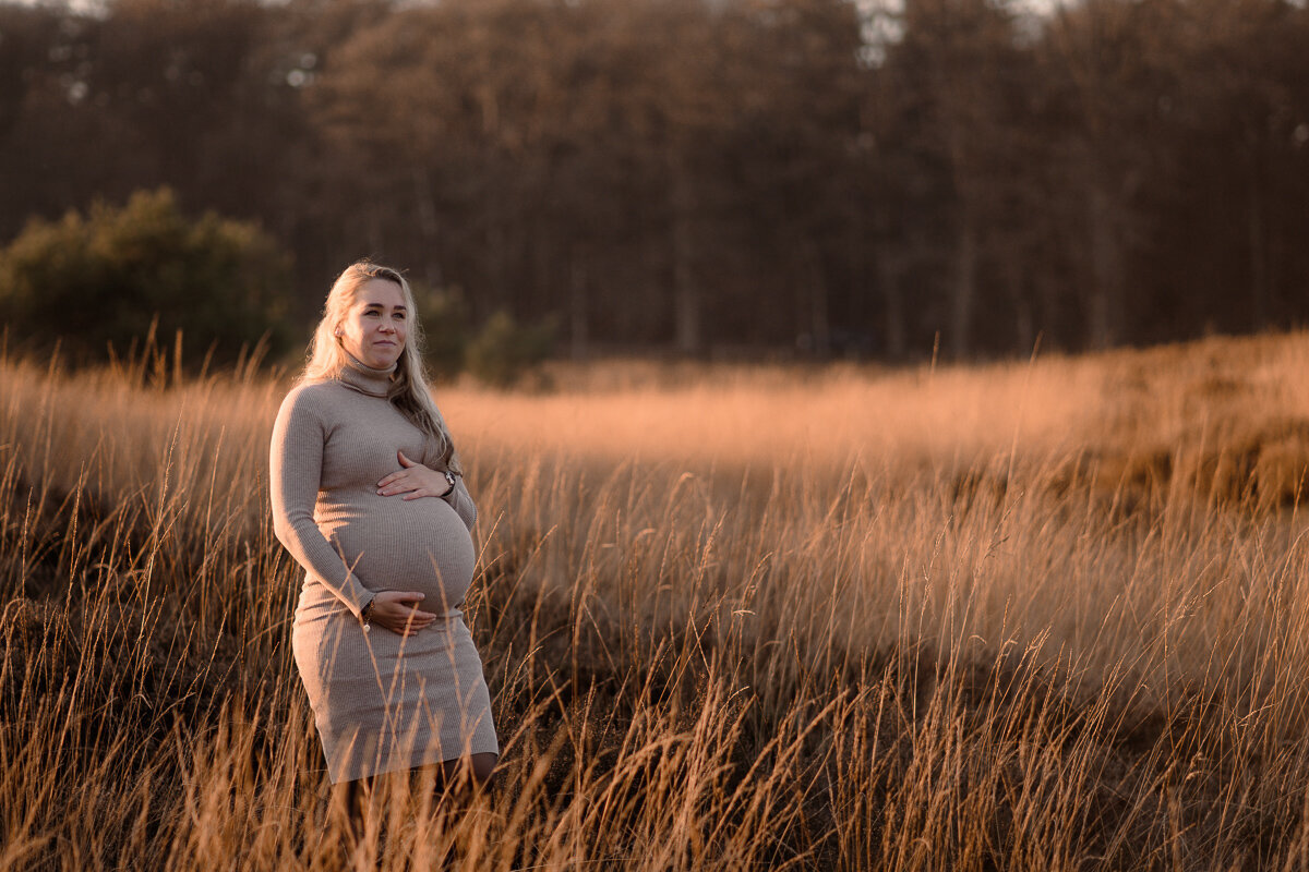 Zwangere vrouw staat in een open vlakte in de zon en kijkt om zich heen