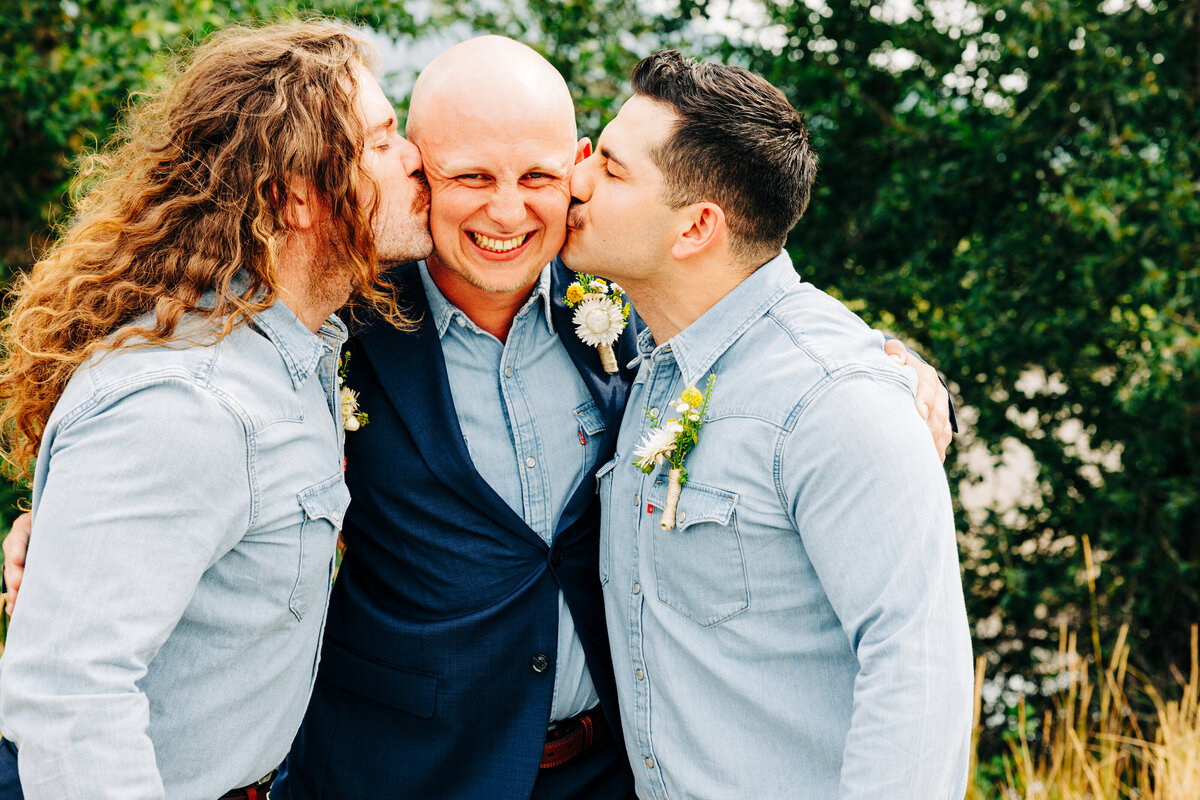 Groomsmen kissing groom on cheek at Miles Park Band Shell in Livingston, MT