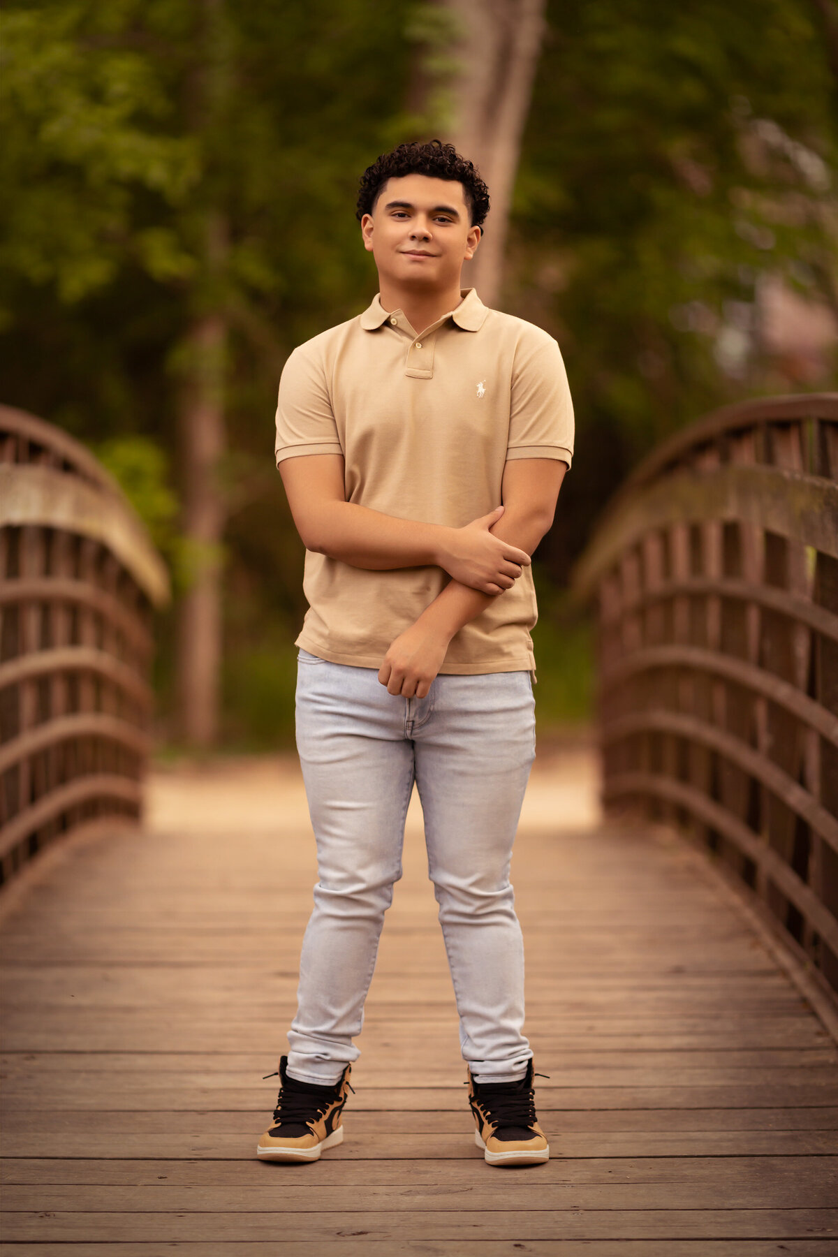 A confident young man poses on a wooden bridge during a family portrait session with Dallas family photographers, dressed in casual spring attire.