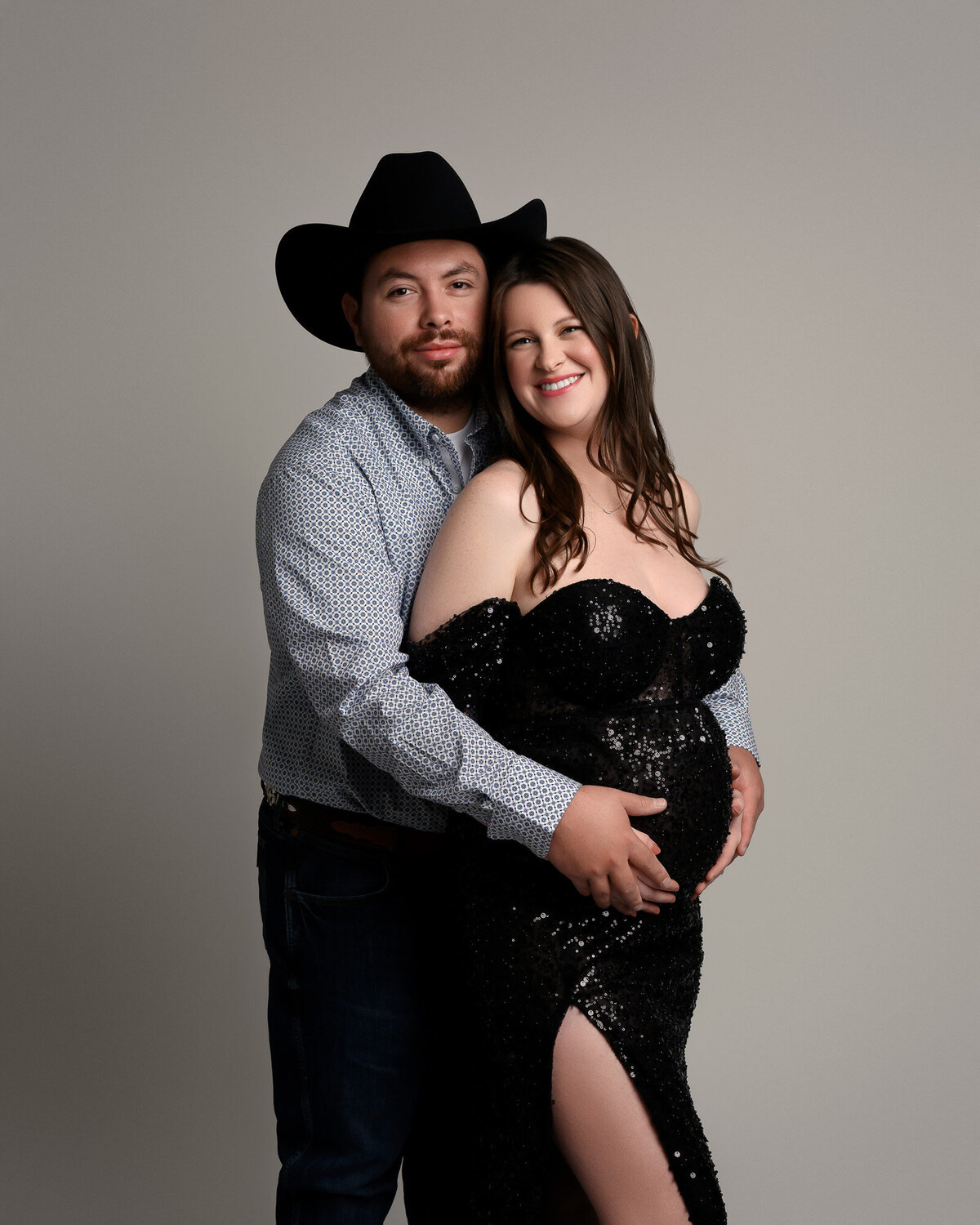 Expecting couple embracing during romantic maternity photography session with soft studio lighting