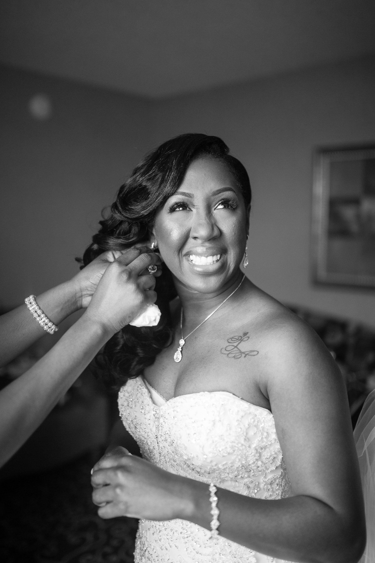 Bride is all smiles as her bridesmaid helps her put on her earrings.