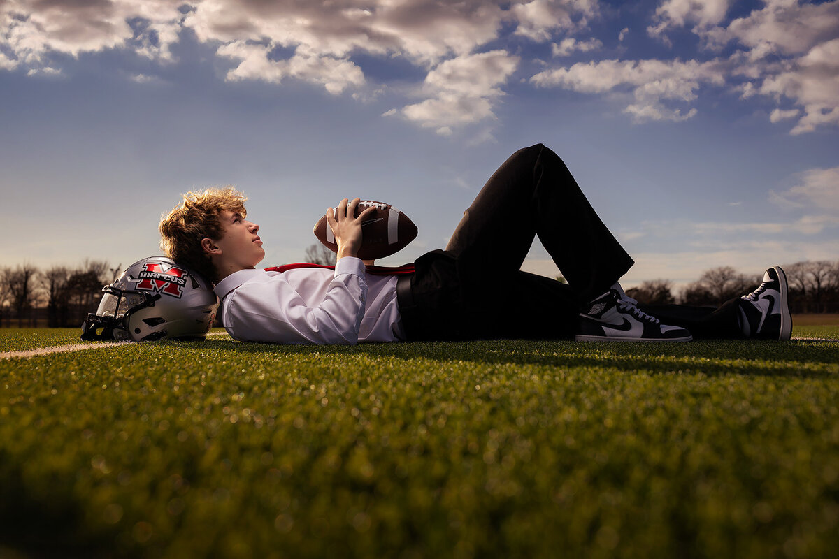 A high school senior in a suit, lying on the football field with a ball, senior photos Dallas.