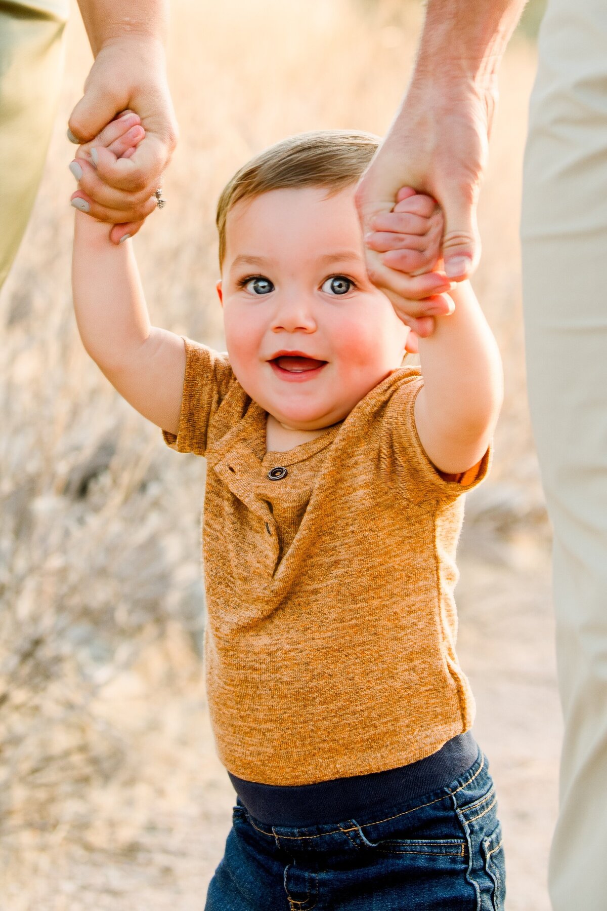 little boy holding his parents hands smiling at the camera