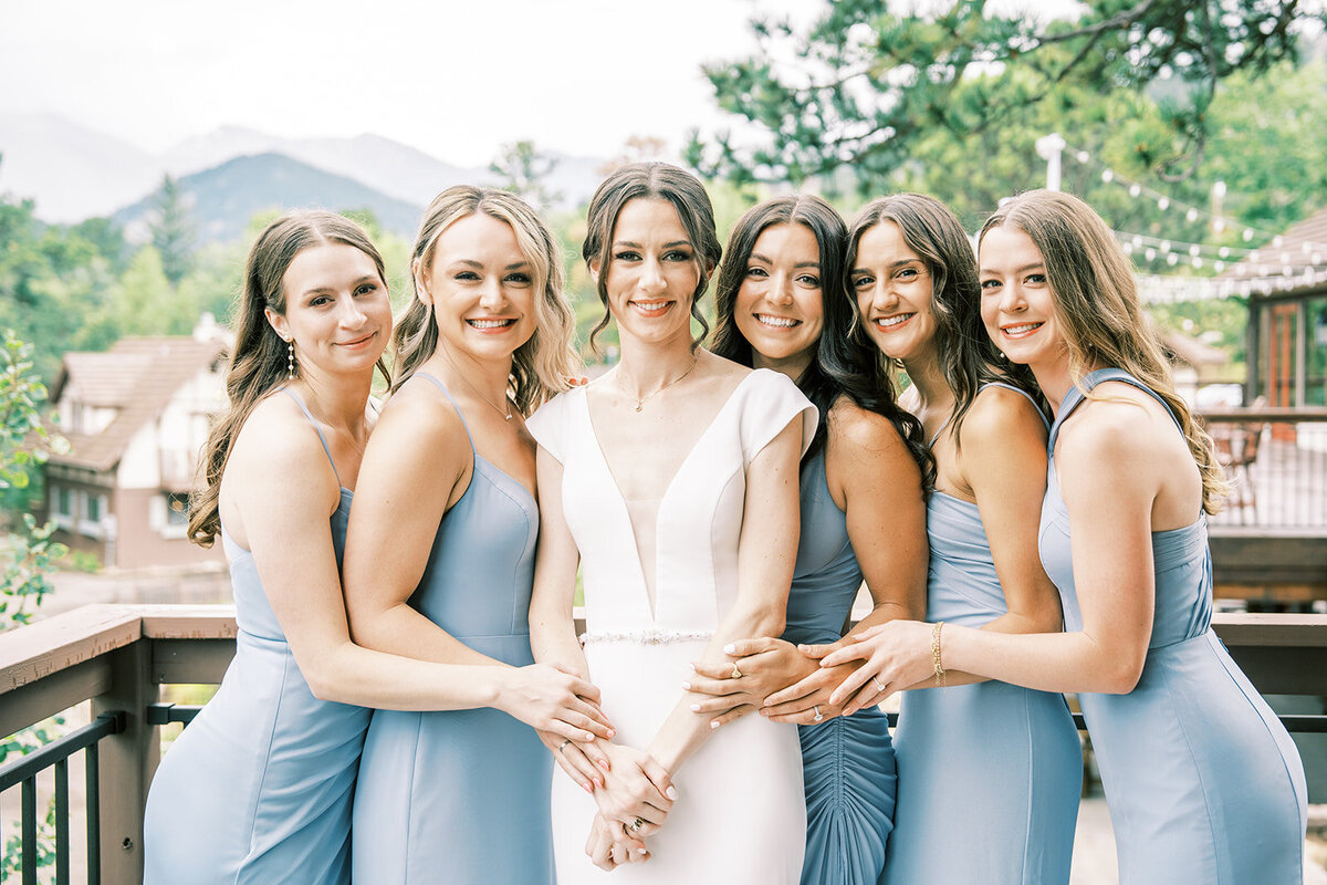 Bride and bridesmaids smile in light blue dresses at the Landing at Estes Park  before the wedding ceremony.