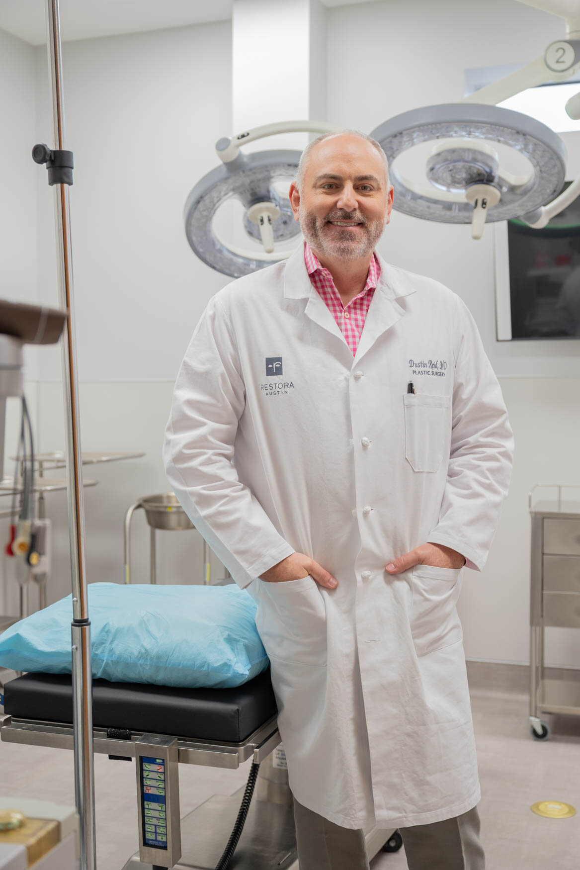 An image of a doctor wearing a white coat standing in the operation room looking and smiling to the camera