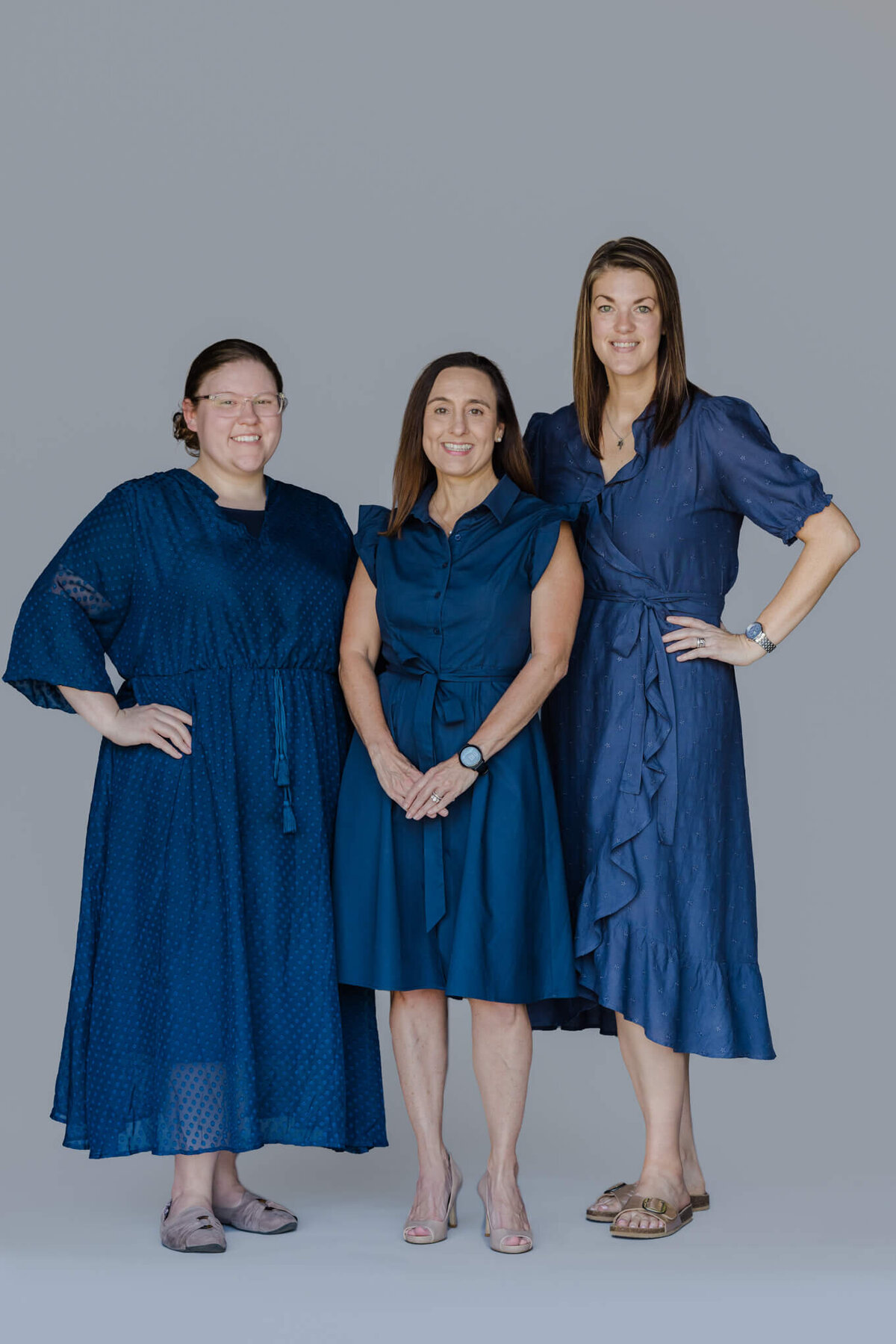 Group portrait of Longview, TX JBA Financial Services staff in navy blue dresses standing in front of light grey backdrop