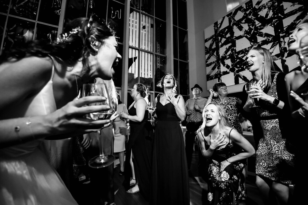 Black and white photography of a bride and one of her guests belting out song lyrics to one another at the Mint Museum Uptown by Charlotte wedding photographers DeLong Photography