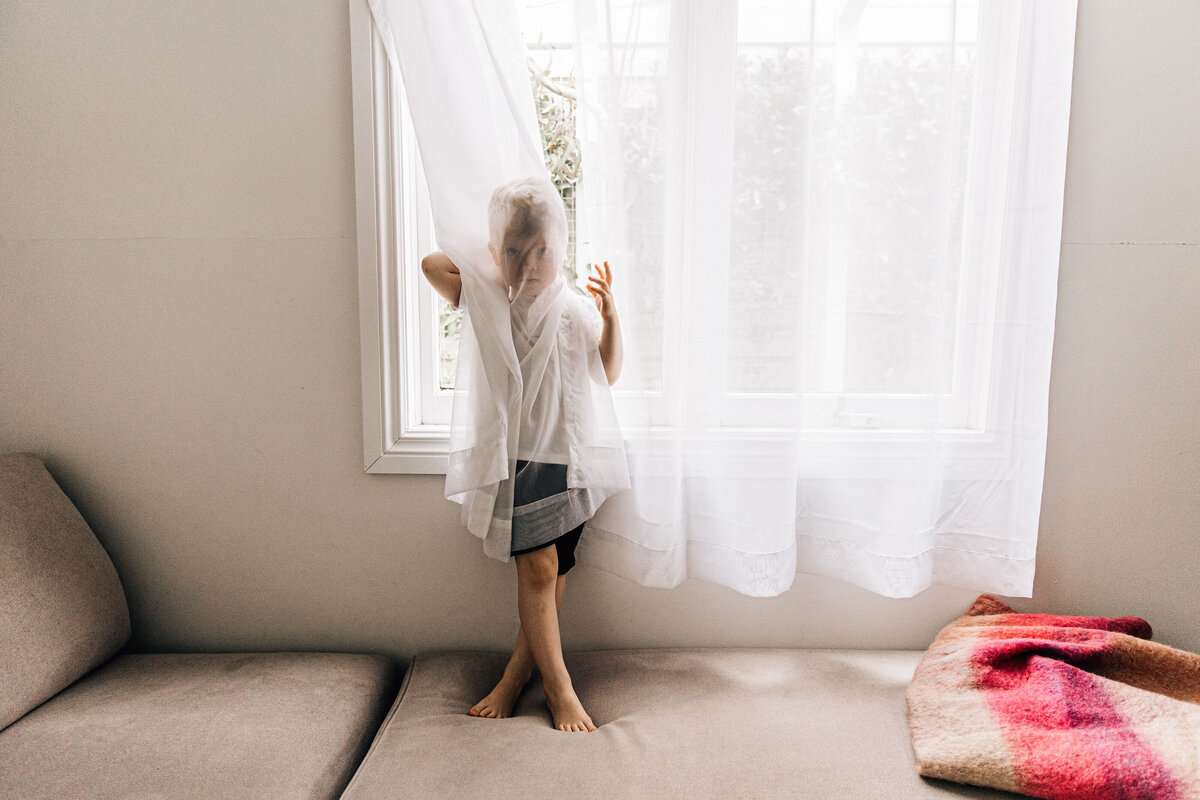 Young boy hides behind sheer curtains