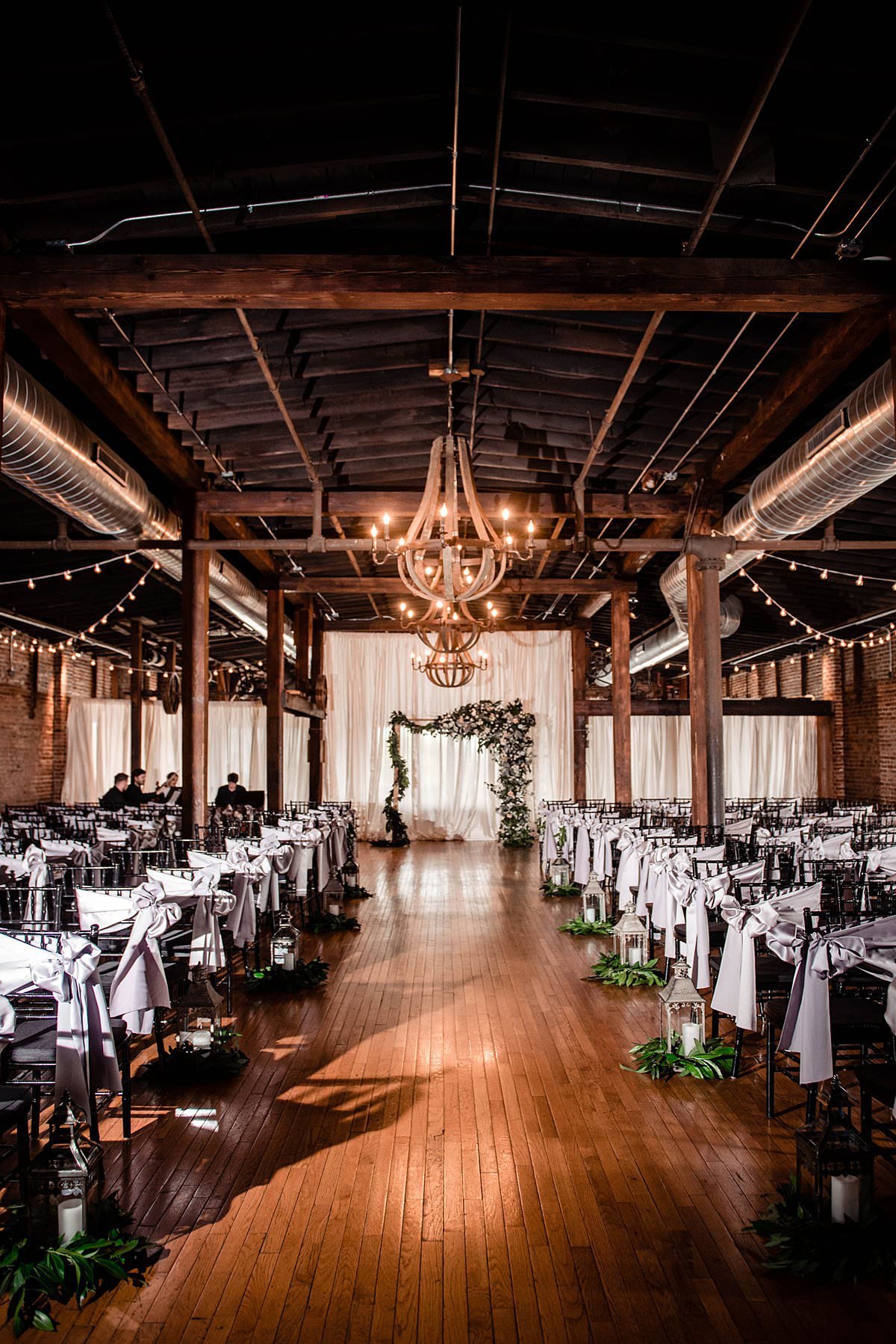 Inside ceremony set up for top floor at Cannery Ballroom showing chairs, chandelier and greenery covered arbor